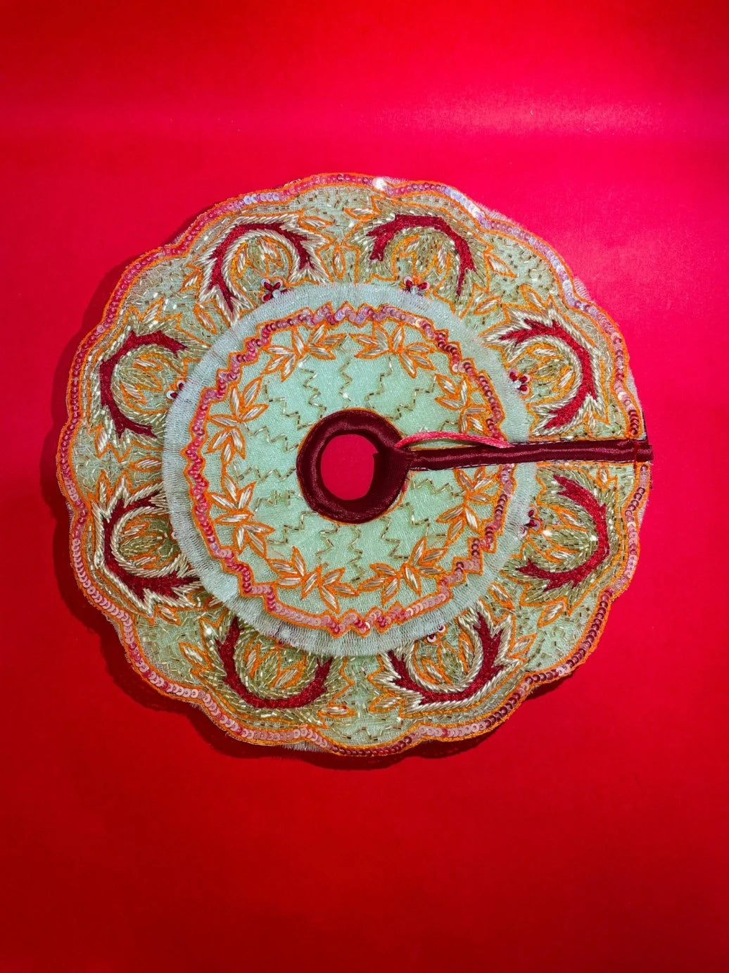 Green and orange embroidered Laddu Gopal dress set with pagdi and patka, displayed on red background and worn by idol.