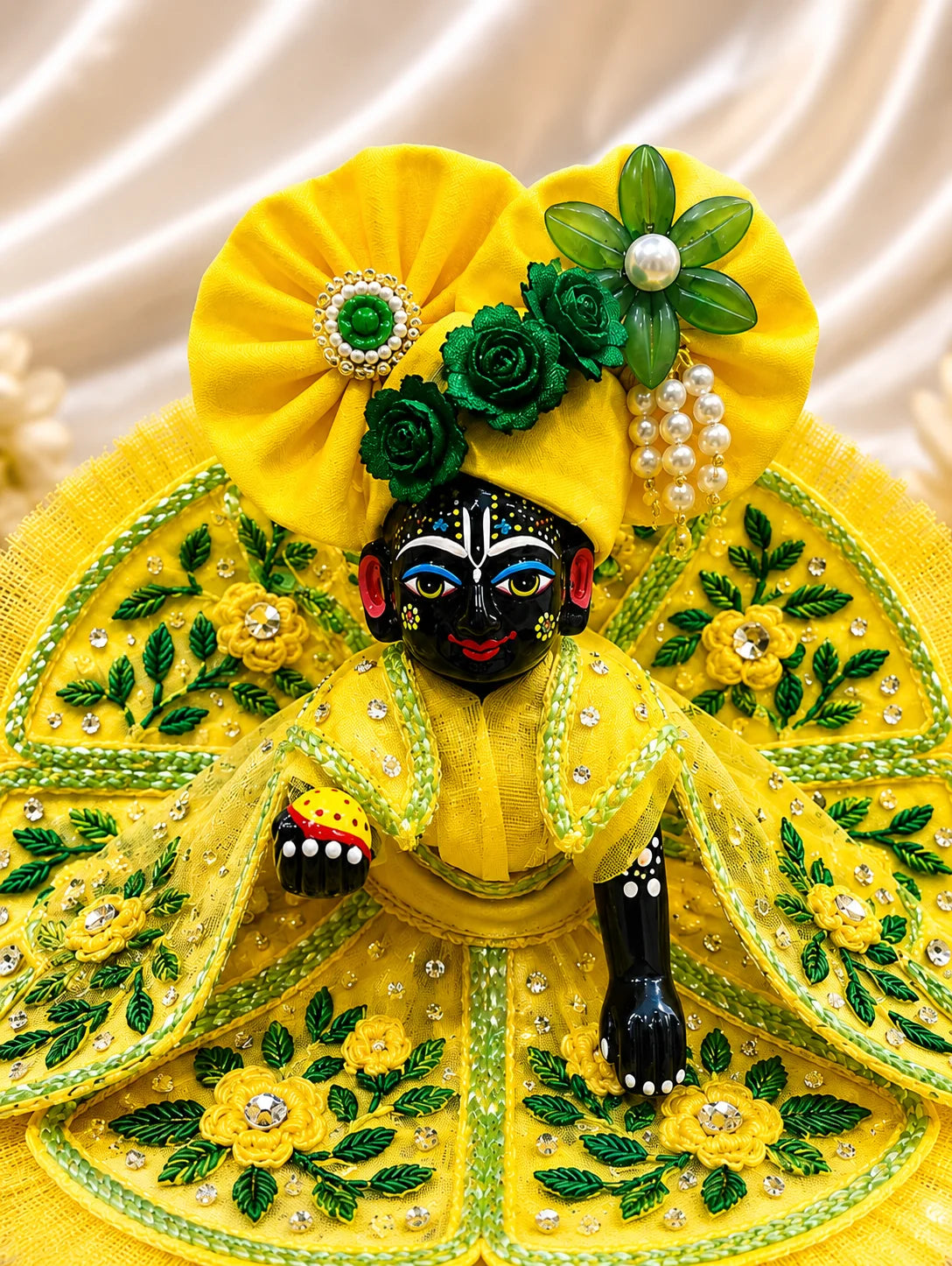 Black stone Laddu Gopal Ji idol adorned in a premium bright yellow dress with green leaf embroidery, sparkling stone work, and a matching heavy yellow turban decorated with green fabric roses