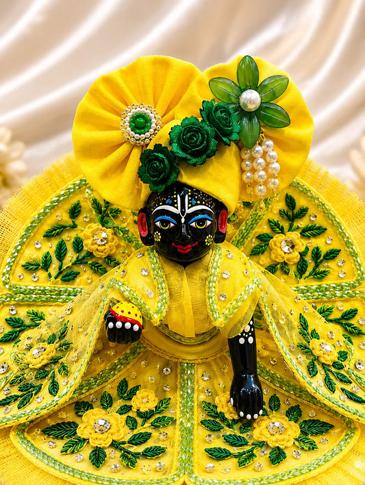 Black stone Laddu Gopal Ji idol adorned in a premium bright yellow dress with green leaf embroidery, sparkling stone work, and a matching heavy yellow turban decorated with green fabric roses