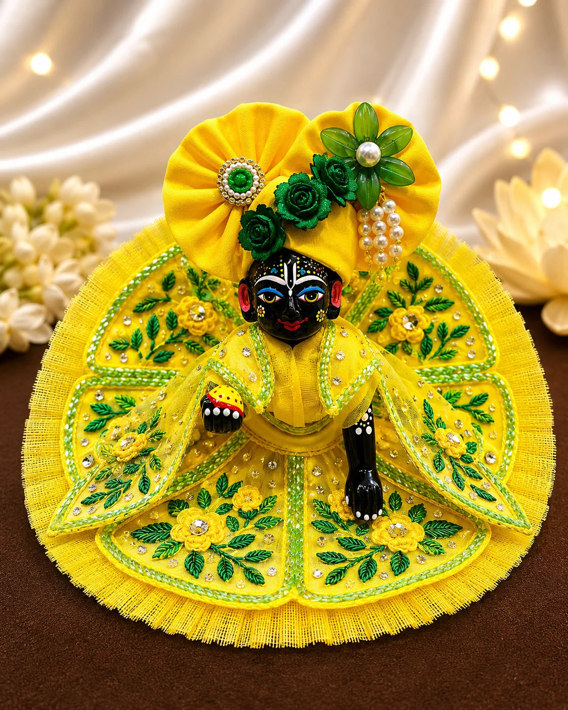 Black stone Laddu Gopal Ji idol adorned in a premium bright yellow dress with green leaf embroidery, sparkling stone work, and a matching heavy yellow turban decorated with green fabric roses