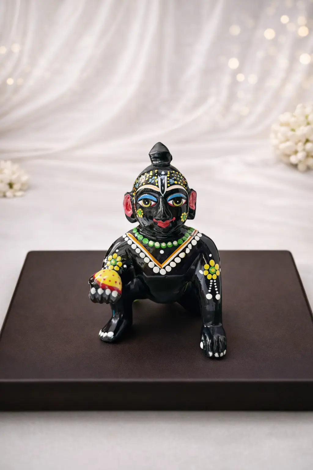 Black Laddu Gopal Vigraha idol holding a laddu – hand-painted brass murti with devotional detailing.