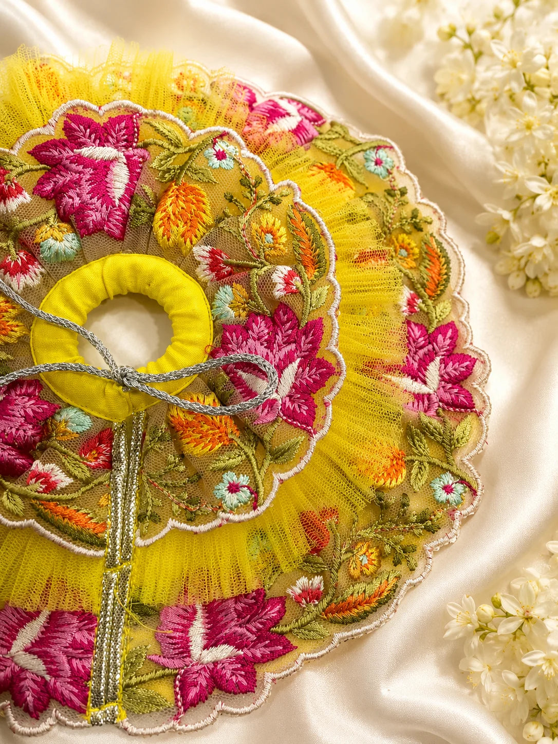 Black stone Laddu Gopal Ji idol wearing a premium yellow double-layered dress with multi-color magenta and orange floral embroidery, silver scalloped lace, and a matching yellow turban decorated with a heavy magenta fabric rose