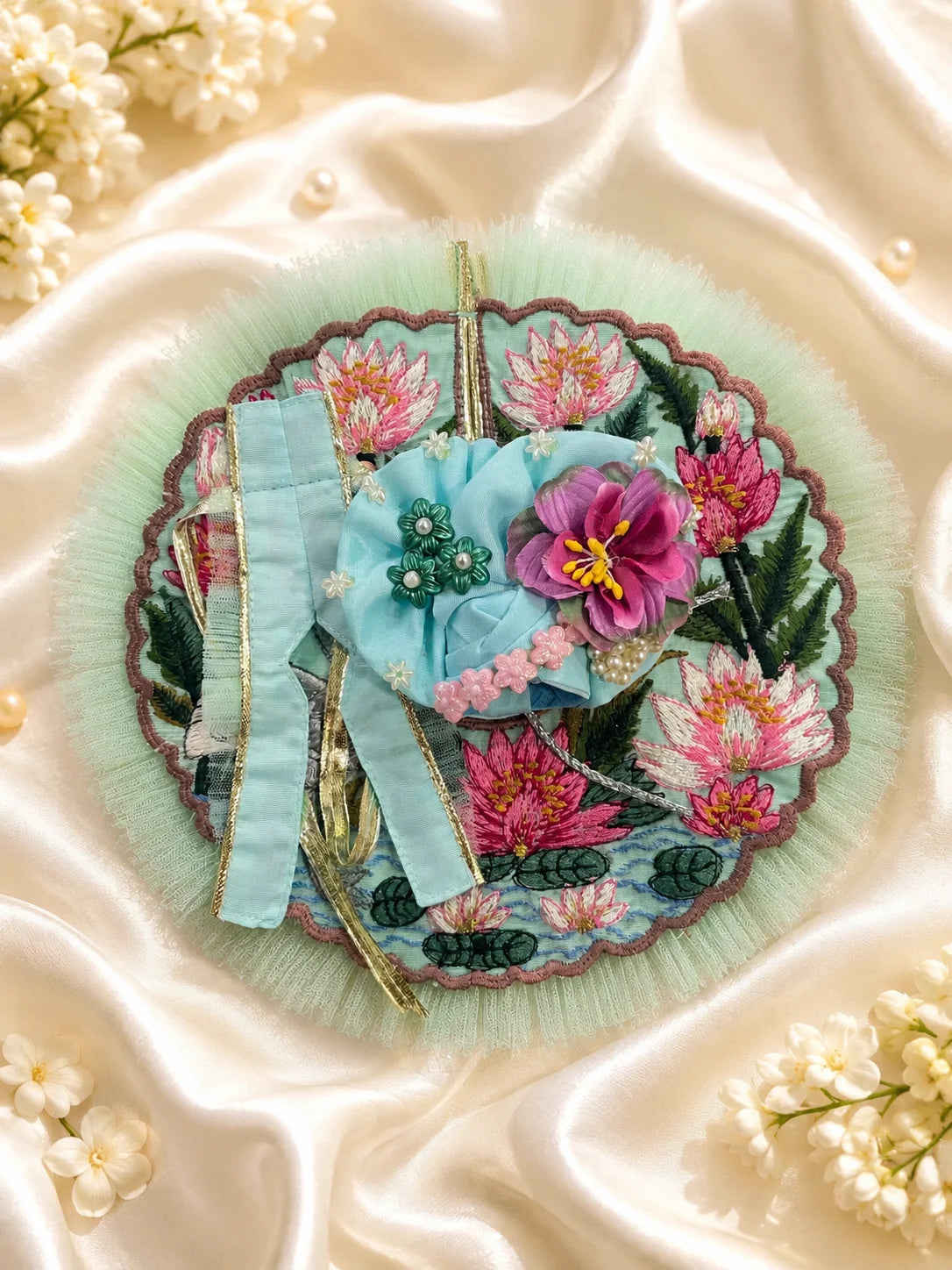 Close-up view of a mint green Laddu Gopal poshak featuring highly detailed embroidery of a white swan, pink lotus flowers, green lily pads, and a scalloped brown border with light green mesh frill&nbsp;