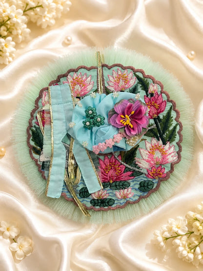 Close-up view of a mint green Laddu Gopal poshak featuring highly detailed embroidery of a white swan, pink lotus flowers, green lily pads, and a scalloped brown border with light green mesh frill&nbsp;
