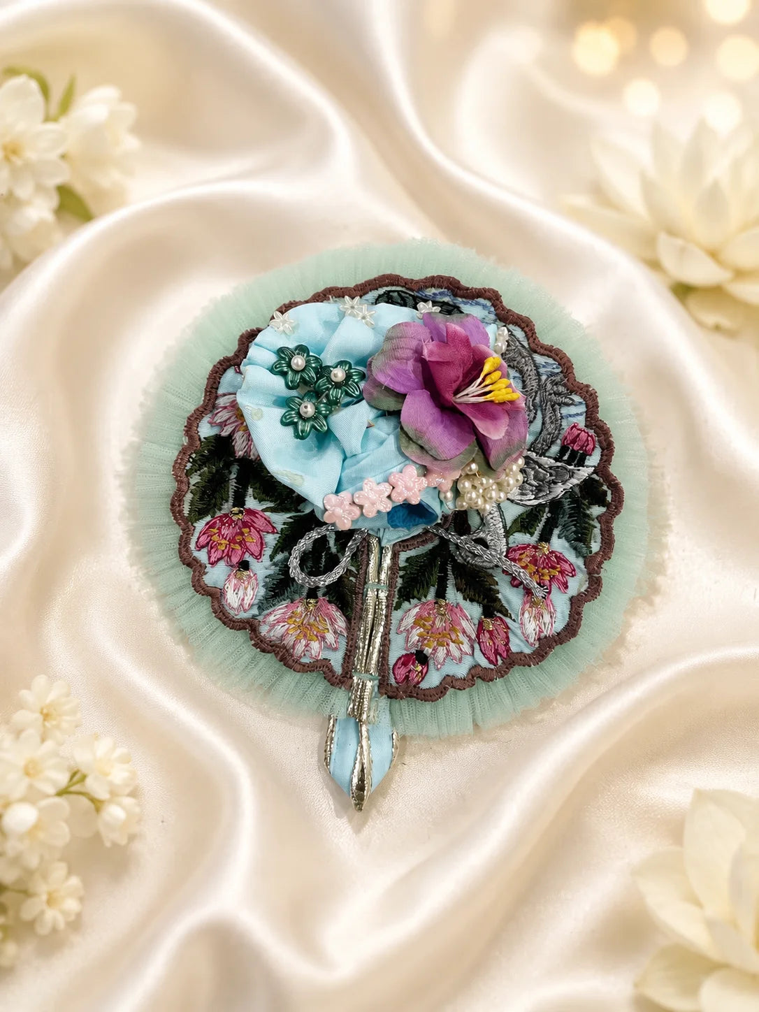 Close-up view of a mint green Laddu Gopal poshak featuring highly detailed embroidery of a white swan, pink lotus flowers, green lily pads, and a scalloped brown border with light green mesh frill&nbsp;