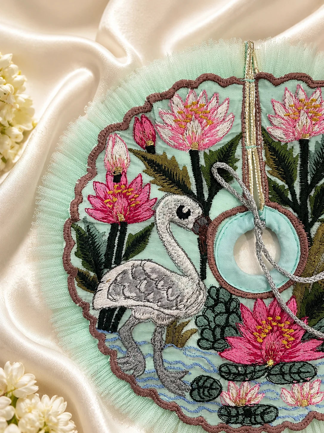 Close-up view of a mint green Laddu Gopal poshak featuring highly detailed embroidery of a white swan, pink lotus flowers, green lily pads, and a scalloped brown border with light green mesh frill&nbsp;