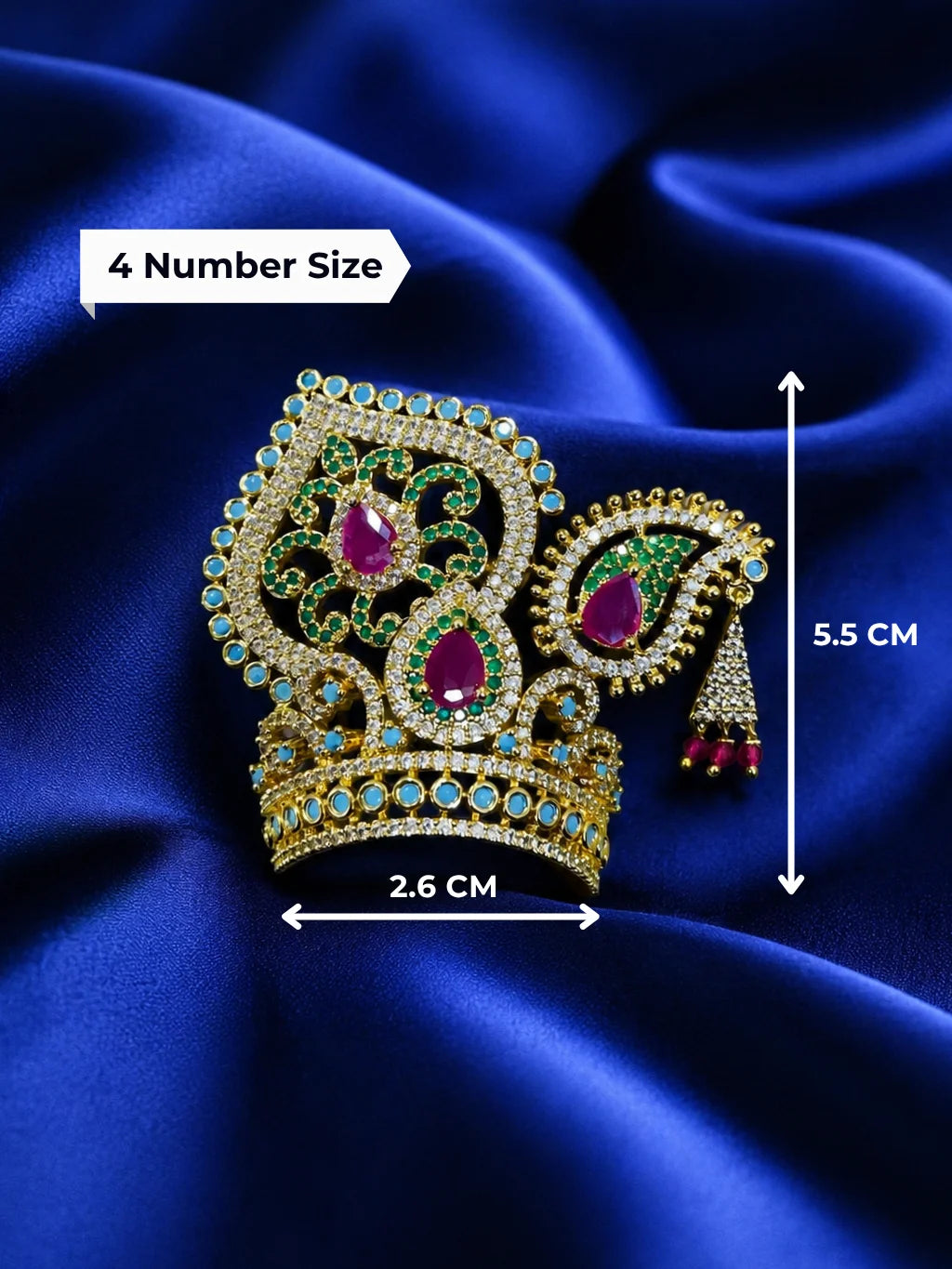 Premium gold-plated Laddu Gopal diamond mukut featuring intricate ruby red and emerald green stone placements on a rich royal blue satin fabric background