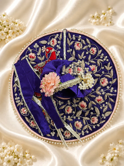 Royal purple Laddu Gopal dress set with detailed silver embroidery, embroidered peacock motif, pearl border, matching patka, and pink flower pagdi turban on white silk fabric