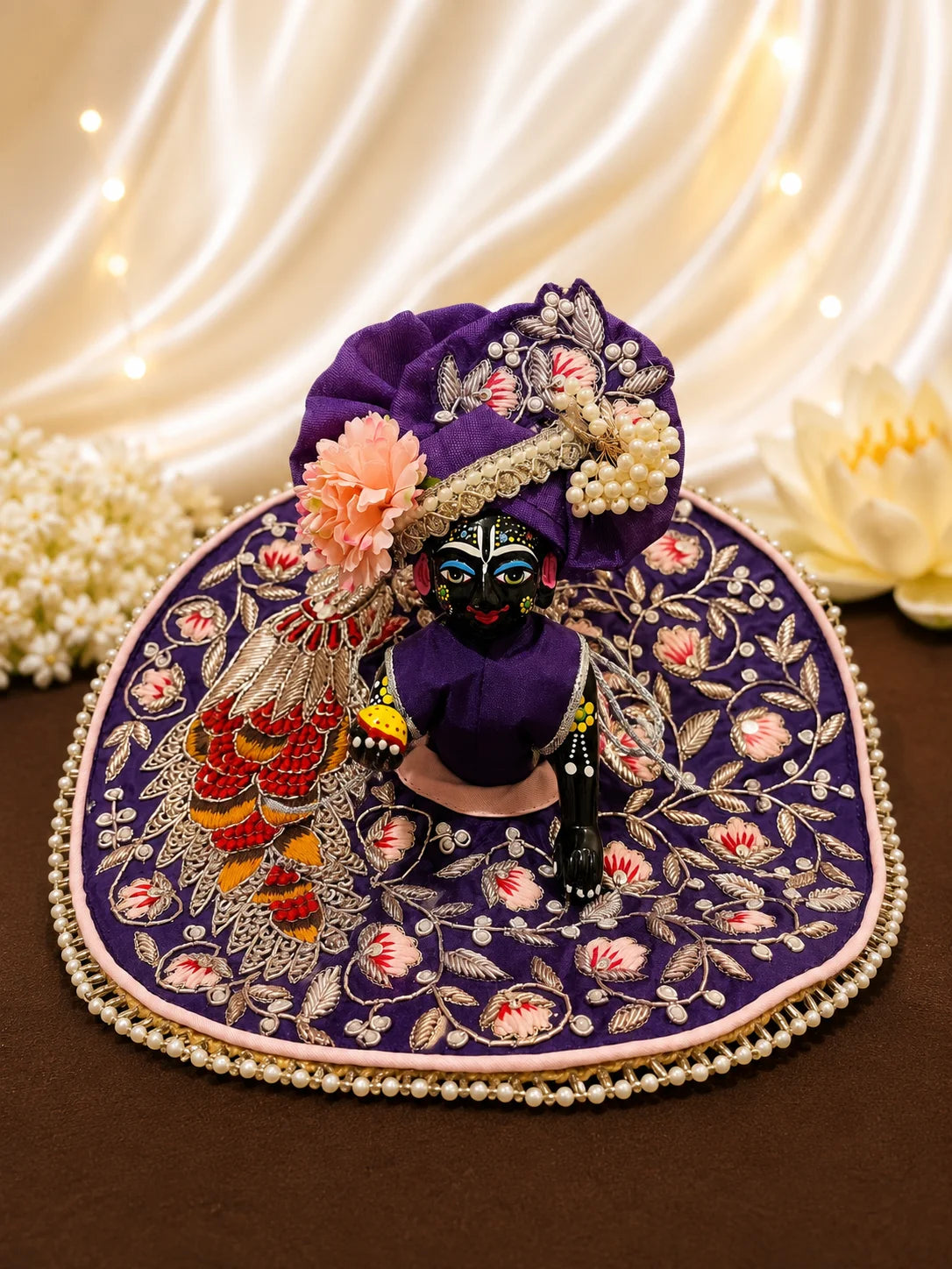 Royal purple Laddu Gopal dress set with detailed silver embroidery, embroidered peacock motif, pearl border, matching patka, and pink flower pagdi turban on white silk fabric
