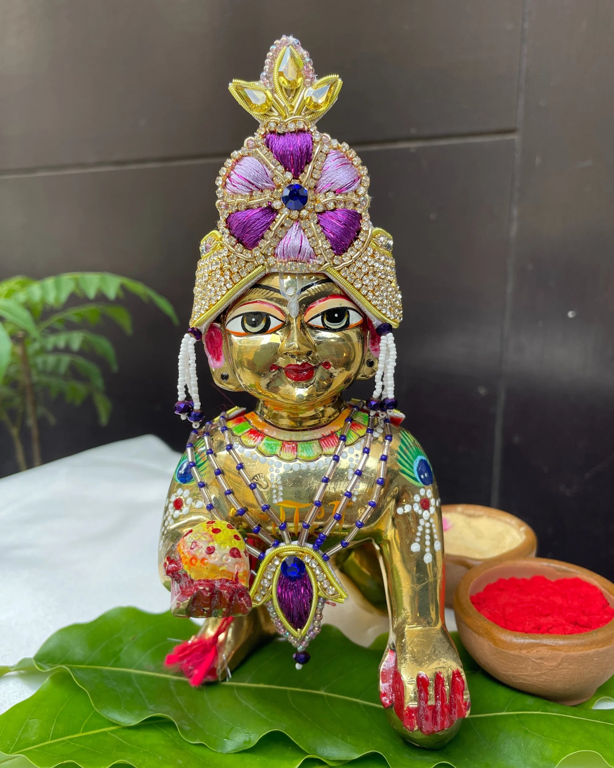 Bal Gopal idol wearing a purple embroidered mukut and layered mala – elegant Laddu Gopal jewellery set for pooja and festive shringar.